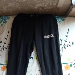 Svarta mjukisbyxor från Hoodrich - Säljer ett par svarta mjukisbyxor från Hoodrich i storlek medium. Byxorna har en avslappnad passform med snörning i midjan och en tryckt logga på ena benet. Perfekta för en chill dag hemma eller ute.