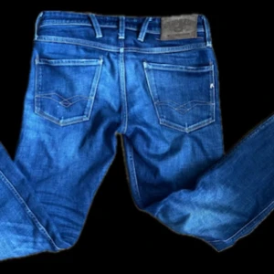 Blå jeans från Replay| W28 L32 - Snygga blå jeans från Replay med klassisk femficksdesign och subtila detaljer. Jeansen har en normal passform och är tillverkade i slitstarkt denim. Några slitningar på fickan där bak men går att fixa