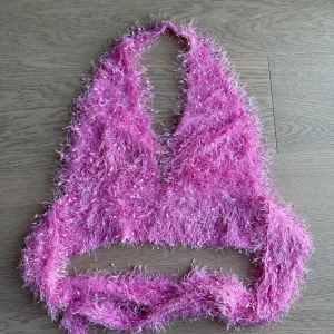 Rosa fluffig topp - Rosa fluffig topp med halterneck-design. Toppen har en glittrig och lurvig textur som ger en festlig känsla. Perfekt för att sticka ut på nästa fest!