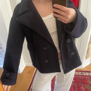 Marinblå kappa med knappar - Säljer en stilren marinblå kappa med dubbelknäppning och bred krage. Jackan har långa ärmar och en klassisk design som passar perfekt för kyligare dagar. Perfekt för dig som vill ha en tidlös look. Obs ej fläckar det är spegeln!! 
