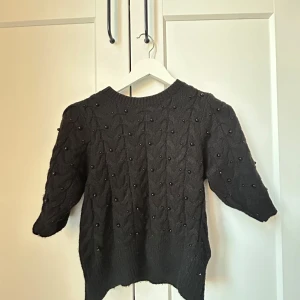Svart stickad tröja med pärlor - Säljer en elegant svart stickad tröja dekorerad med små pärlor. Tröjan har trekvartsärmar och en rund halsringning. Hör av dig vid intresse!