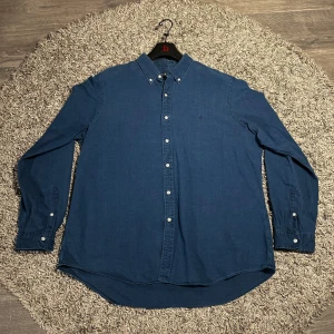 Ralph Lauren skjorta (nyskick) - Säljer en snygg svart skjorta från Ralph Lauren i storlek XXL passform som XL. Skjortan har långa ärmar och knappar framtill samt en broderad logotyp på bröstet. Perfekt för en stilren look! Det ör en Indigo oxfort i ett material liknande jeans! Nypris ligger på 1800kr ish och den är fortfarande i nyskick som sagt. Hör av er vid frågot svarar på allt! Finns flera skjortor att kolla på min sida. MVH Wilmer