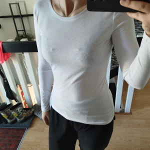 Vit långärmad topp - Säljer en stilren vit långärmad topp med rund hals. Perfekt för lager-på-lager eller att bära som den är. Passar till både jeans och kjol för en enkel och snygg look.