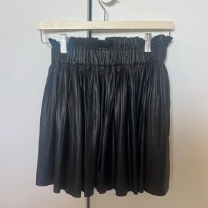 Svart kjol i skinnimitation -  svart kortkjol i skinnimitation med elastisk midja för en bekväm passform, den har även inbyggda shorts under. Passar bra till både vardag och festliga tillfällen.🫧