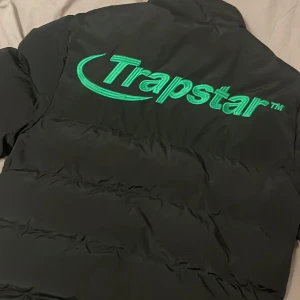pufferjacka från Trapstar - Säljer en svart pufferjacka från Trapstar med grönt logotryck på bröstet och ryggen. Jackan har en dragkedja framtill och två fickor med knappar. Perfekt för kyliga dagar. Har defekter finns på bilderna, finns även ett litet hål inuti jackan men märks inte när man har på, är lite smutsig men allt går bort i tvätten priset kan alltid diskuteras 