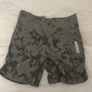 Grå camo shorts från Gymshark - Snygga grå camo shorts från Gymshark med hög midja. Perfekta för träning med en tight passform som ger bra stöd. De har en elastisk midja och är gjorda i ett bekvämt syntetmaterial.