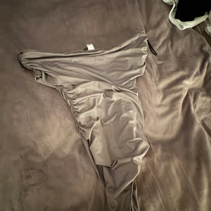 Beige offshoulder body - Snygg beige body glansigt material med offshoulder-modell och rynkade detaljer längs sidorna. Materialet känns mjukt och följsamt mot huden.