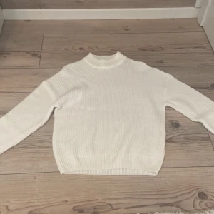 Vit stickad tröja från FB Sister XS - Vit ribbstickad tröja från FB Sister i storlek XS. Tröjan har en högre krage och långa ärmar, perfekt för lager-på-lager. Enkel och clean design som funkar till många olika stilar.