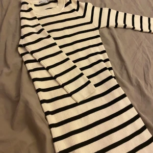 Randig ribbad klänning i svartvitt - Snygg ribbad klänning från Bik Bok i vitt med svarta horisontella ränder. Modellen är kroppsnära med lång ärm och liten slits nertill. Perfekt för dig som gillar en enkel men trendig look.