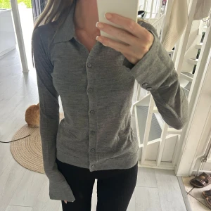 Grå långärmad skjorta i ull - Snygg grå skjorta med lång ärm och klassisk krage. Skjortan har knappar hela vägen framtill och är tillverkad i mjuk ull, vilket gör den både bekväm och stilren. Perfekt till svarta byxor eller jeans för en clean look. Från nakd 