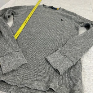 Grå stickad tröja från Polo Ralph Lauren - Säljer en grå stickad tröja från Polo Ralph Lauren med klassisk rund hals och långärmad modell. Tröjan har ribbade muddar och det ikoniska broderade logotypen på bröstet. Perfekt för lager-på-lager och chill stil.