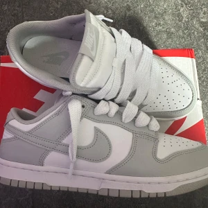 Nike Dunk Low i vitt och grått - Hej, säljer dessa tvärfeta skor från Nike dunks kollektionen. De är bara använda en gong och sitter på storlek 42 i mäns storlekar. De är specialgjorda med extra stora vita snören vilket gör de lite mer loose, alltså skönare. För mer bilder kan ni gärna skriva, priset kan även diskuteras.