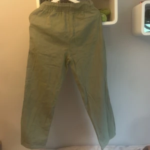 Gröna linnebyxor från H&M, strl 152 - Snygga ljusgröna linnebyxor från H&M i storlek 152. Byxorna har resår i midjan, sidfickor och en bakficka. Perfekta för en chill och avslappnad stil, tillverkade i svalt linnematerial. Passar dig som gillar bekväma och stilrena plagg.