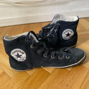  Converse skor i mocka - Svarta fodrade Converse All Star sneakers i mocka. Klassisk rund tå, svarta snören och vita detaljer längs sulan. Ikonisk logga på sidan och All Star-märke bak. Perfekta för kyligare dagar med sin varma insida.