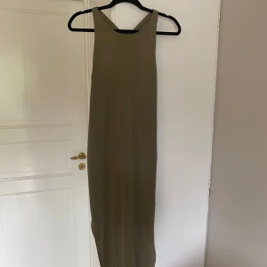 Olivgrön långklänning från Superdry - Snygg olivgrön långklänning från Superdry med ärmlös design och rund halsringning. Klänningen har en slits på båda sidorna. Perfekt för dig som gillar minimalistisk stil och vill ha något bekvämt men ändå trendigt. Klänningen har en maska på baksidan men inget som märks tydligt, kom privat för bild på det! Annars är klänningen i fint skick men har använts en del. Hör gärna av er vid frågor!💕