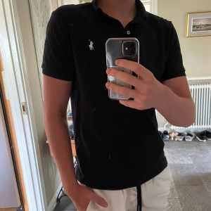 Mörkblå pikétröja Ralph Lauren  - Mörkblå pikétröja från Ralph Lauren i custom slim fit. Klassisk design med korta ärmar, krage och knappar framtill. Ikoniska broderade loggan i vitt på bröstet. Tillverkad i mjuk bomull som är skön mot huden.