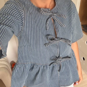 Randig peplumblus med knyt från Ganni - Supersöt blå och vit randig peplumblus från Ganni med tre knyt framtill och volang nertill. ❣️❣️❣️