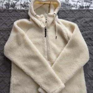 Offwhite fleecehoodie från Everest - Mysig offwhite fleecehoodie från Everest i storlek S. Tröjan har huva med dragsko, half zip-dragkedja och är tillverkad i fluffigt teddyfleece-material. Perfekt för kyliga dagar och riktigt skön att dra på sig när det är kallt ute.