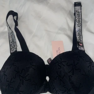 Svart glittrig bh från Victoria's Secret från Dubai, påsen ingår  - Supersnygg svart bh från Victoria's Secret med VS-logga i sammet över hela tyget. Axelbanden är täckta av glittrande stenar och har textdetaljer. Perfekt för dig som vill ha något extra under outfiten.