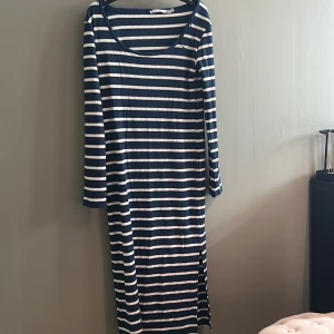 Randig långklänning från 157 - Snygg långärmad långklänning från 157 i marinblått och vitt med horisontella ränder. Klänningen är ribbad och har en rundad halsringning samt slits i sidan. Perfekt för dig som gillar en avslappnad men stilren look.