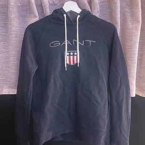 Marinblå hoodie från GANT med tryck - Snygg marinblå hoodie från GANT med vit snörning i huvan och broderad logga, använd några få gånger. 