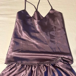 Lila satin pyjamas med shorts och linne - Nypris 120 kr aldrig använda Snygg lila pyjamas i glansigt satinmaterial med smala axelband och v-ringad hals. Pyjamasen har en avslappnad passform och ett lätt rynkat midjeparti för en cool och trendig look. 