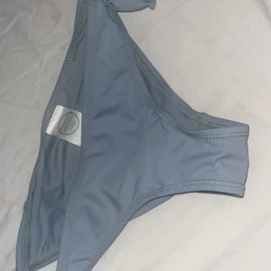 Ljusblå bikini från Swim Girl - Supersöt ljusblå bikini från Swim Girl med klassisk trekantsmodell och knyt i sidorna. Enkel och stilren design som passar perfekt till stranden eller poolen. Materialet är mjukt och stretchigt för en bekväm passform.