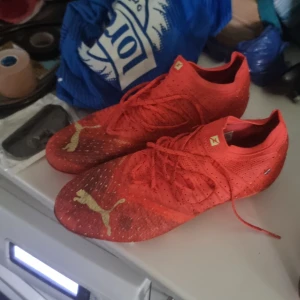 Röda fotbollsskor från Puma - Snygga röda fotbollsskor från Puma med guldiga loggor på tån. Skorna har snörning och är tillverkade i ett lätt syntetmaterial med ventilerande mesh för bästa komfort på planen.