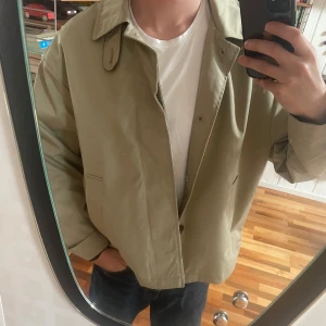 Beige rock - Säljer en lite oversize stilren beige (lite grönaktig) rock. Jackan har klassisk krage, raka fickor och knäppning framtill. Insidan har ett diskret rutigt foder. Perfekt för dig som gillar en clean och tidlös look. Passar perfekt till kallare sommardagar eller till hösten och vintern. Aldrig använd. Nypris 799 kr