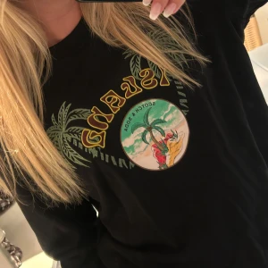 Svart tröja Scotch & Soda Island print - Svart långärmad tröja från Scotch & Soda med färgglatt Island-tryck framtill. Motivet har palmer, strand och text i gult. Tröjan har rund hals och relaxed fit, perfekt för en chill och cool look. Nypris runt 1000kr.