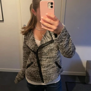 Gråmelerad cardigan jacka från Lindex - Säljer en gråmelerad cardigan jacka från Lindex med svart dragkedja och snygga svarta detaljer. Jackan är stickad och har lång ärm, perfekt för lager-på-lager. Passformen är normal och materialet känns mjukt och mysigt. Storlek M men passar mig som bär XS/S.