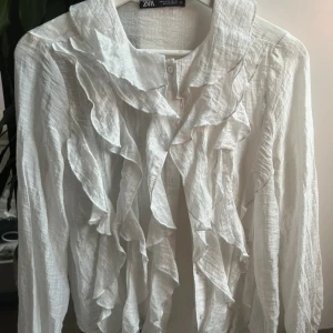 Vit volangskjorta från Zara, stl S - Supersnygg vit skjorta från Zara med volanger framtill och längs kragen. Lätt och luftig känsla!