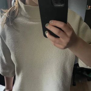 Beige polotröja i frotté - Säljer en vit polotröja i mjukt frottématerial. Tröjan har boxig passform, halvlånga ärmar och hög krage som ger en chill vibe. Perfekt för dig som gillar minimalistisk stil och vill ha något bekvämt men ändå snyggt. Köpte för något år sedan och har tyvärr tröttnat på den, är använd ganska lite men har haft på mig den några gånger. Snygg, modern och stilig och hoppas att någon kommer ha en bra användning av den. Inga skador på tröjan och rdinarie pris 400 sek. Finns ej längre att köpa i butik.