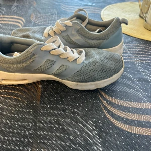 Blå sneakers  - Snygga grå sneakers med mesh-ovandel och vita detaljer. Skorna har vita snören och en vit sula med bra grepp. Perfekta för dig som gillar en sportig och clean stil. Lätta och bekväma för vardagsbruk.