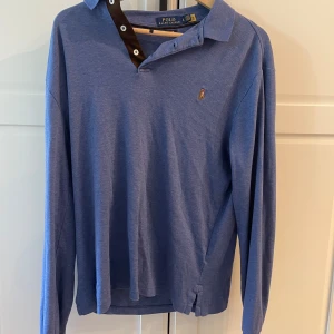Blå pikétröja Polo Ralph Lauren - Snygg blå långärmad pikétröja från Polo Ralph Lauren i slim fit. Tröjan har klassisk krage, knappar vid halsen och den ikoniska broderade loggan på bröstet. Tillverkad i 100% bomull för en skön och lätt känsla.