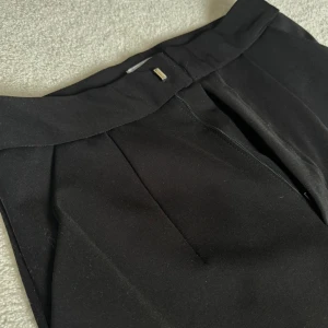 Svarta wide kostymbyxor MN Shop - Snygga svarta kostymbyxor från MN Shop vida ben. Byxorna har klassisk dragkedja framtill och stilrena pressveck. Perfekta för en clean och trendig look.