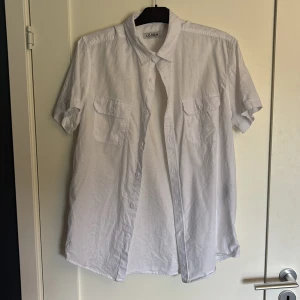 Vit kortärmad skjorta från Lodon - Vit skjorta från Lodon i luftig bomull, perfekt för varma dagar. Klassisk krage, korta ärmar och två bröstfickor med knappar. Rak passform och knäppning framtill. Enkel och stilren design som funkar till många olika looks.