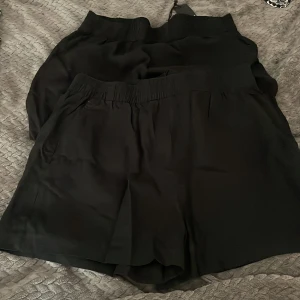 Svarta loose shorts med resårmidja - Säljer ett par svarta shorts med loose fit och bred resår i midjan. De är enkla och stilrena, perfekta för chill dagar eller när du vill ha något bekvämt. Materialet känns lätt och svalt, vilket gör dem grymma för varmare dagar.