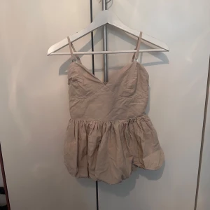 Beige volangig linnetopp  - Supersöt beige linnetopp med justerbara smala och avtagbara axelband och volangig, bubblig nederdel. Perfekt för sommaren! Från Misay i storlek S.