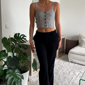 Randig top - Superfin croppad top från Topshop i grått och vitt randig. Toppen har breda axelband, knappar framtill och en figurnära passform. Perfekt till höga byxor eller kjol för en trendig look. Lappen kvar.