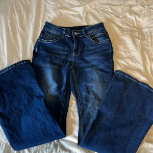 Mörkblå bootcut jeans med kontrastsömmar - Snygga mörkblå jeans med bootcut passform och tydliga vita kontrastsömmar. Klassisk femficksmodell med dragkedja och knapp framtill. Jeansen har en lätt tvättad look och är perfekta för dig som gillar en tidlös stil.