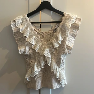 Beige spetsblus med volang från Zara - Supersöt beige blus från Zara med virkade detaljer och breda spetsvolanger längs v-ringningen och axlarna. Blusen är ärmlös med romantisk känsla och har en figurnära passform. Perfekt för dig som gillar vintagevibbar och unika detaljer. Storlek är M Dock är självaste modellen en liten typ så den passar perfekt till midjan för alla längder. 290kr plus frakt!