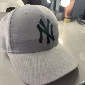 Vit New York Yankees keps - Snygg vit keps från 47 Brand med klassiskt New York Yankees-logo broderat i svart framtill. Justerbar rem baktill med Yankees-text. Orginalpris ligger på 300-400kr. Den är helt oanvänd. Vid frågor är det bara att höra av sig!💞