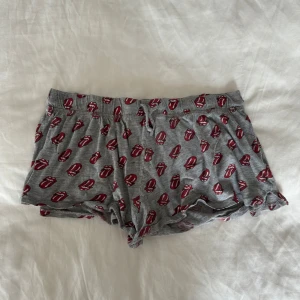 Grå pjamas shorts med Rolling Stones-tryck - Grå mjuka shorts med Rolling Stones-tryck i rött och vitt över hela plagget. De har elastisk midja och avslappnad passform, perfekta som pyjamasshorts🤩