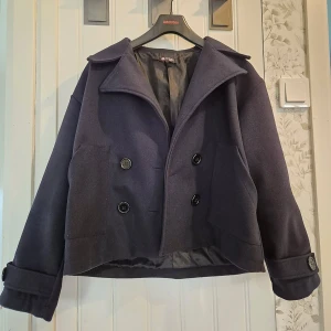 Mörkblå kappa - En mörkblå kappa från Chelsea som passar till alla olika tillfällen. Perfekt nu till sommaren och hösten.