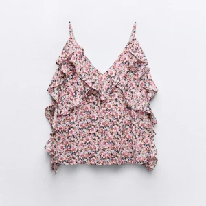 Blommig volangtop med smala axelband - Supersöt blommig linnetopp med volanger och smala axelband. Toppen har v-ringning och ett färgglatt mönster i rosa, vitt och grönt. Perfekt för varma dagar när du vill känna dig extra somrig och söt.