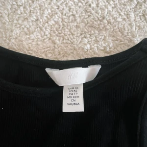 Svart ribbad klänning från H&M XS - En svart, tight ribbad klänning från H&M i storlek XS. Klänningen är enkel och stilren med rak passform och stretchigt material som sitter snyggt på kroppen. Perfekt för dig som gillar minimalistisk stil och vill ha en klänning som funkar till många tillfällen.