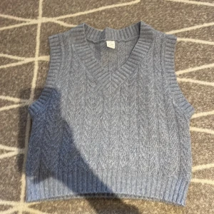 Grå stickad väst från Lindex Kids - Säljer en grå stickad väst från Lindex Kids i storlek 134/140. Västen har ett klassiskt kabelstickat mönster, bred ribbad kant vid halsringning, ärmhål och nederkant. Perfekt att slänga över en skjorta eller t-shirt för en chill och snygg look.