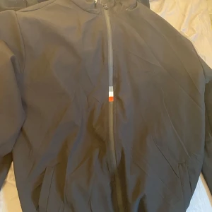 Svart vindjacka från Moncler - Snygg svart vindjacka från Moncler med klassisk logga på ärmen och hel dragkedja framtill.  Obs! Rep