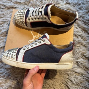 Christian Louboutin sneakers  - Unika sneakers från Christian Louboutin i svart och vitt med röda detaljer. Skorna har canvas och skinn, snörning och coola silverfärgade nitar på tån. 7/10 skick. Allt og kommer med, finns kvitto för de som vill se bild. Extra spikar kommer med. Kvittot är dock borttappat så de kommer ej med. Bara att skriva vid minsta fundering! 